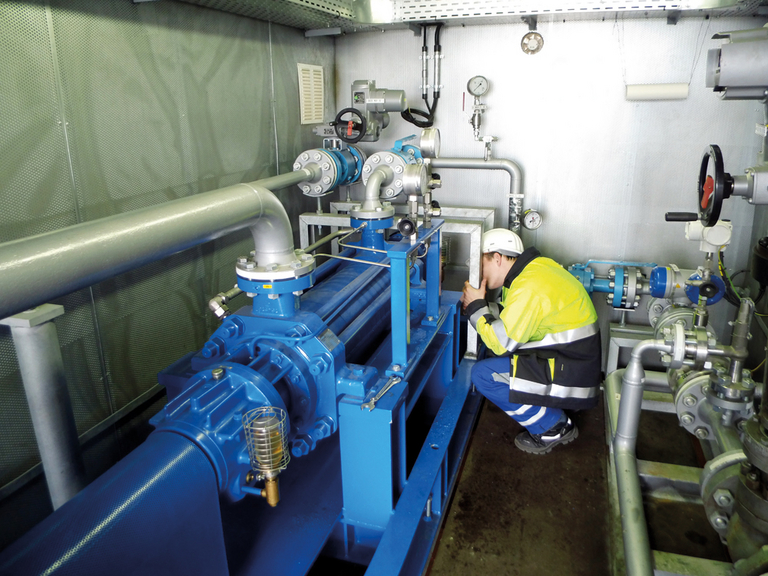 Service personnel on their knees in front of an industrial pump, checking the system, which is located in a container