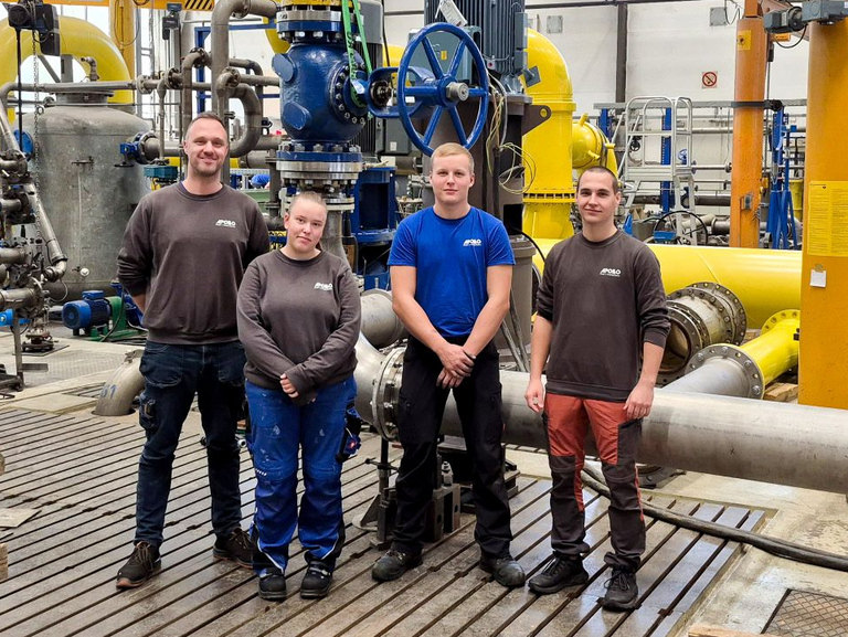 Group photo of two instructors standing next to a female trainee and a male trainee in front of the Apollo pump test stand.