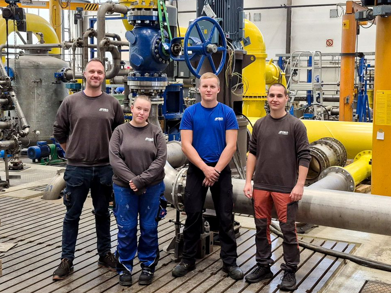 Gruppenbild von zwei Ausbildern an der Seite von einer Auszubildenen und einem Azubi vor dem Apollo Pumpenprüfstand.