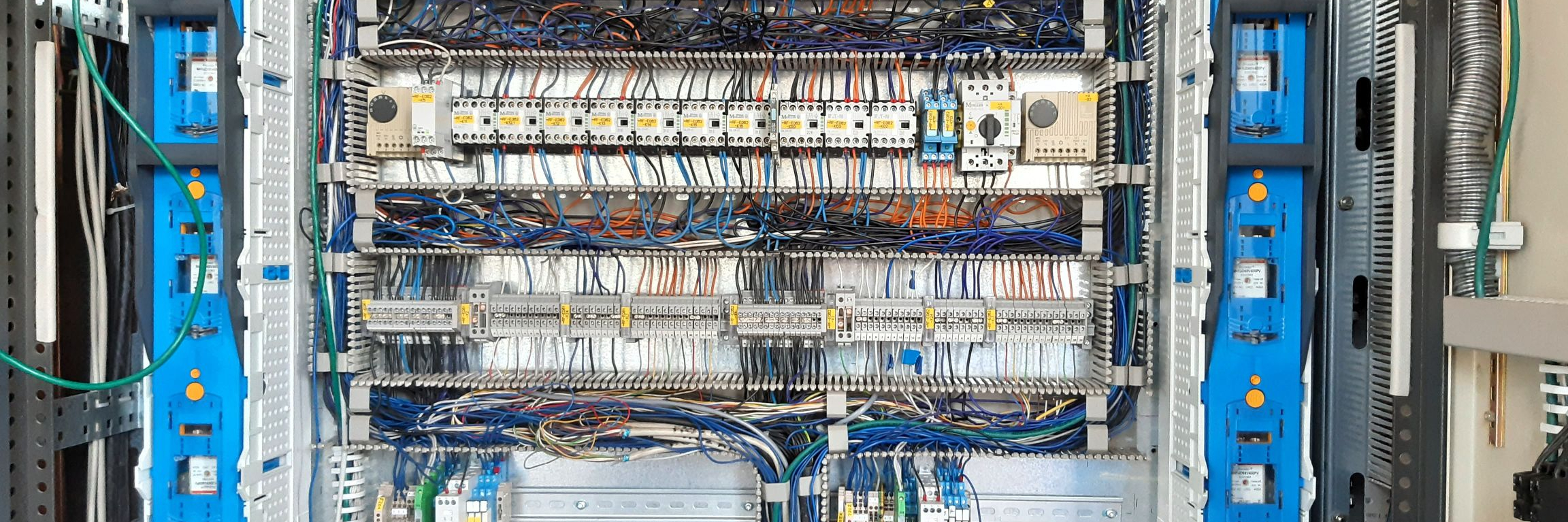 Zu sehen ist ein Apollo-Schaltschrank, ein Schaltschrank einer Pumpenanlage, in Frontansicht mit geöffneten Türen. Zu sehen sind die Leistungs- und Steuerungskomponenten, darunter Sicherungsleisten und Klemmenreihen. Alle Komponenten sind sauber strukturiert und eindeutig beschriftet.