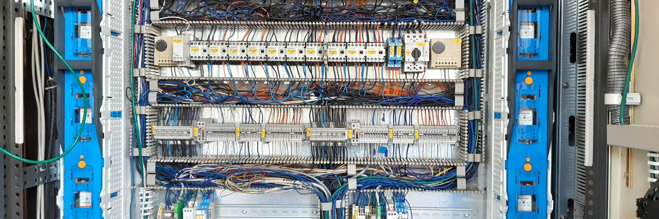 The image shows an Apollo control cabinet, a control cabinet for a pump system, viewed from the front with the doors open. The power and control components are visible, including fuse strips and terminal strips. All components are neatly structured and clearly labeled.
