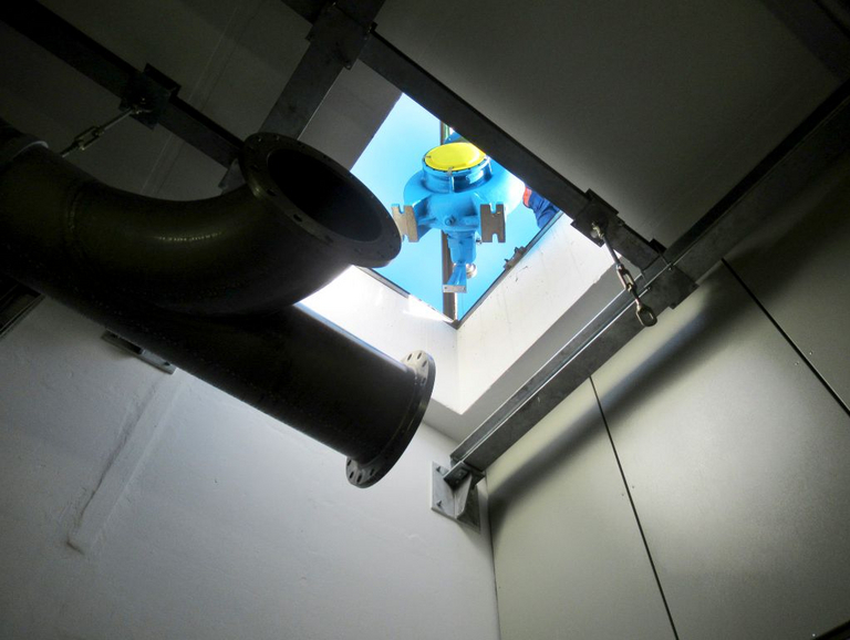 Eine blau lackierte KRS-Pumpe hängt am Kran und wird durch eine Bodenluke in die unterirdische Anlage hinabgelassen.