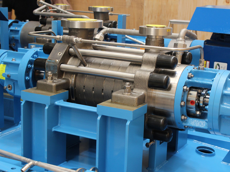 Technische Nahaufname einer Apollo HPB Hochdruckpumpe, welche später als SRU Feed Pumpe eingesetzt wird. Im Hintergrund sind Holzkisten zu sehen sowie ein zweites Pumpenaggregat.