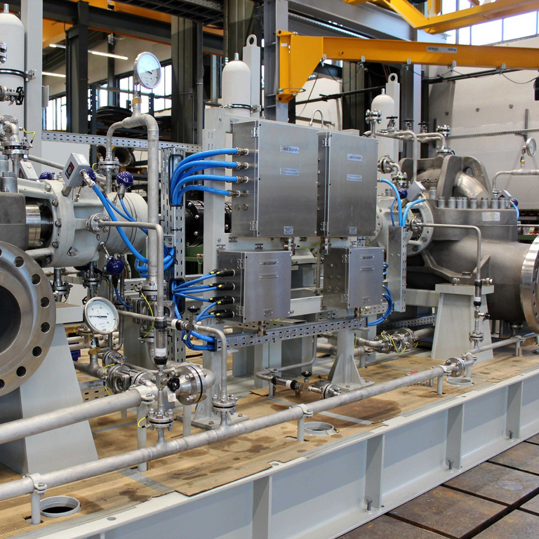 View of the hydraulic power recovery turbine (HPRT) unit with a BB1 pump in the foreground, followed by piping and cabling with switch boxes and then a reverse-running, axially split, single-stage process pump of the ZMK type (BB1 according to API 610).