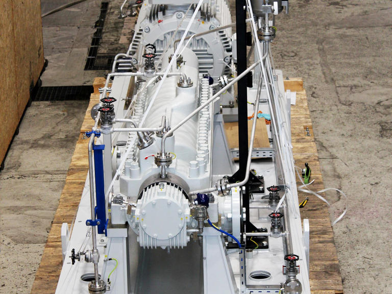 Blick von oben auf das montierte Pumpenaggregat mit allen Komponenten und Zubehörteilen wie Motor und Schmierölsystem. Das Aggregat steht auf einem hölzernen Verpackungsboden bereit für die Endabnahme und ist von Werkstattausrüstung und Produktionsumgebung umgeben.