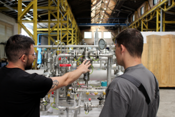 AnlagenbauMontage Ausbilder erklärt einem Auszubildenden die Arbeitsschritte an einem Metallbauteil direkt am Werkstück.