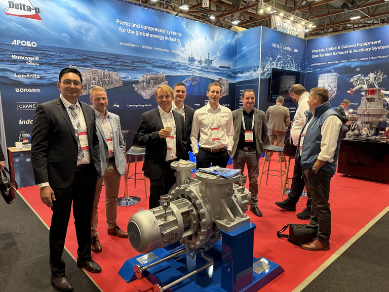 Eine Gruppe von acht Personen steht lächelnd nebeneinander auf dem ONS-Messestand des Partners Delta-p und blickt direkt in die Kamera. Im Vordergrund ist eine Apollo Gößnitz BB2-Prozesspumpe als Ausstellungsstück platziert. Der Hintergrund zeigt eine großflächige Wandgestaltung des Messestandes mit einer Meereslandschaft, einer Offshore-Plattform und mehreren technischen Detailbildern zur Pumpentechnik.