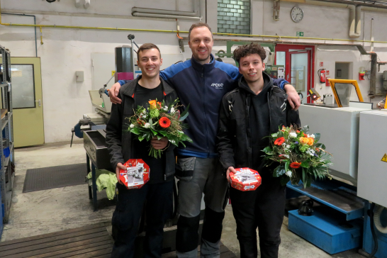 Ausbildungsverantwortlicher umarmt zwei Azubis die beide einen Blumenstrauß in der halten und alle freuen sich, da die Azubis Ihre Prüfung bestanden haben.