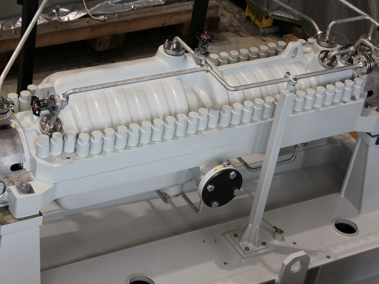 View from above of the gray-painted pump housing with the screw connections of the axially split housing in the Apollo Gößnitz production hall. Workshop equipment and the production environment can be seen in the background. 